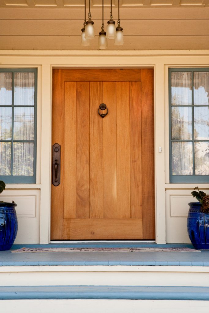 A wide, wooden front door on an upscale home with view of side panel windows. Vertical Shot.